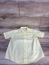 Light yellow kids button-up shirt with short sleeves and chest pocket, laid on wood floor