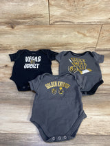Flat lay of three baby bodysuits showing Vegas Golden Knights logos and prints on grey and black fabric on wood background