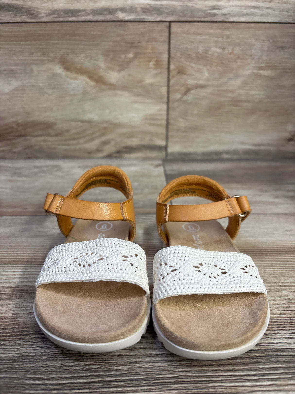 Front view of Cat & Jack toddler Blair strap footbed sandals showcasing tan ankle straps and white crocheted toe bands on wood floor background