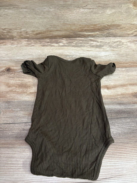 Front view of Kate Quinn green ribbed modal bodysuit, size 3 to 6 months, showcasing short sleeves on wood