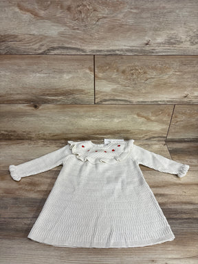 White knitted long-sleeve baby dress with ruffled collar and red embroidered accents on wood background