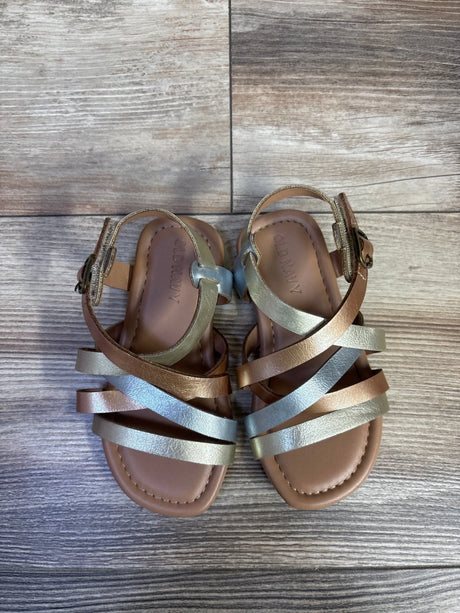 Top view of Old Navy toddler metallic sandals size 7C showcasing crisscross silver, gold, and bronze straps with ankle buckles on light wood floor