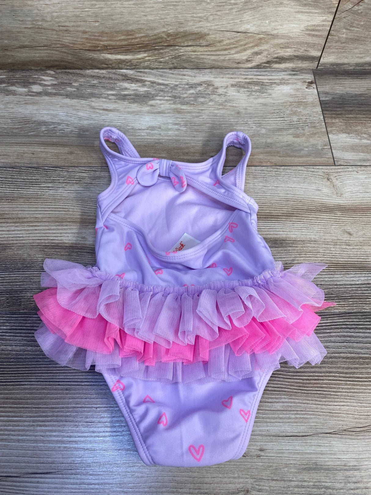 Flat-lay of purple one-piece toddler swimsuit with layered pink and lavender tulle tutu and pink heart print on wood floor