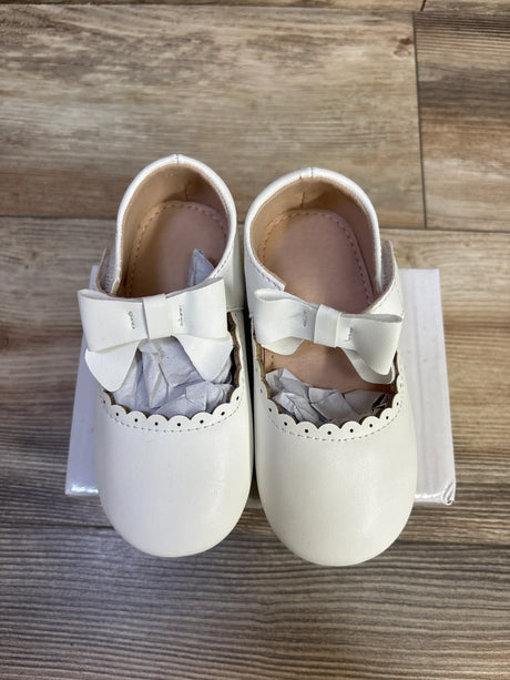 Top-down view of white leather baby princess flats size 7C showing bow straps and scalloped trim on a white box over wood floor