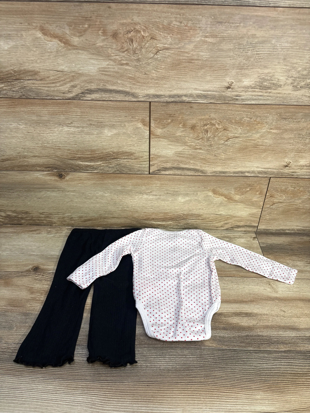 Flat-lay of Hello Kitty 2pc bodysuit and pants (12 months) showing white polka-dot bodysuit and black pants on wood floor
