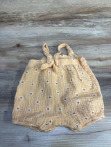 Front flat-lay of orange gauze baby romper with embroidered white daisies, knotted shoulder straps, and elastic leg openings on wood background