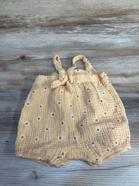 Front flat-lay of orange gauze baby romper with embroidered white daisies, knotted shoulder straps, and elastic leg openings on wood background