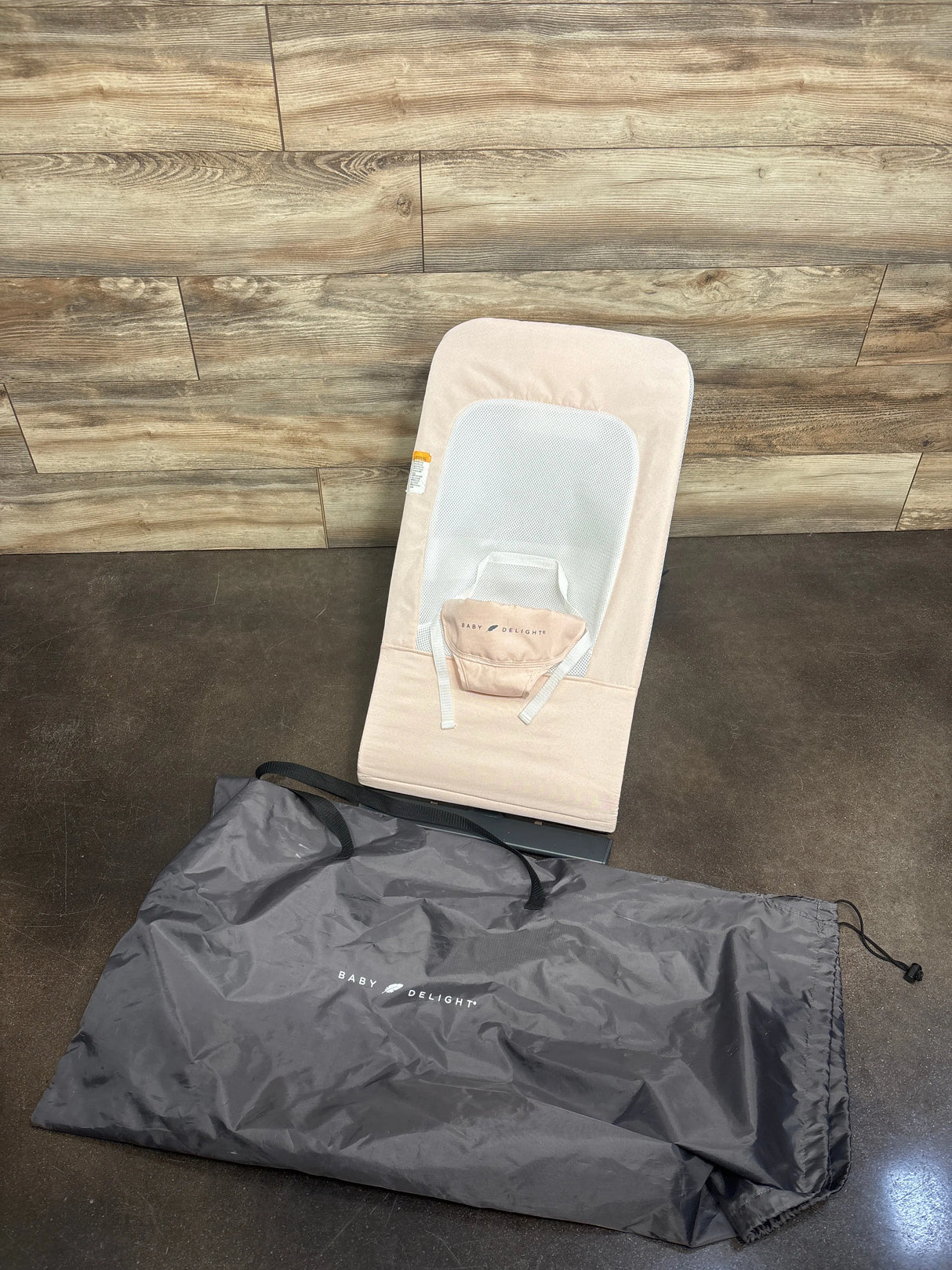 Top-down view of Baby Delight Alpine Deluxe bouncer, pale pink, showing mesh seat, safety harness and included gray carry bag