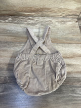 Top-down view of beige newborn corduroy shortalls showcasing crossed back straps and elasticized waist and leg openings on a wood background