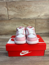 Front view of Nike Dunk Low sneakers in pink and white with perforated toe and white laces on red Nike box on wood floor