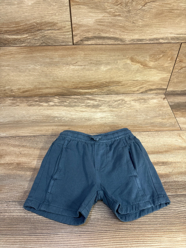 Top down view of blue Zara toddler shorts showing elastic waistband, front pockets, and rolled hems on wooden background