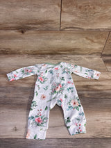 Flat lay of newborn white floral coverall with mint trim showing long sleeves and fold-over cuffs on wood background