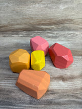 Three-quarter view of Lovevery solid wood stacking boulders, 5-piece set of faceted colorful wooden blocks on a light wood surface