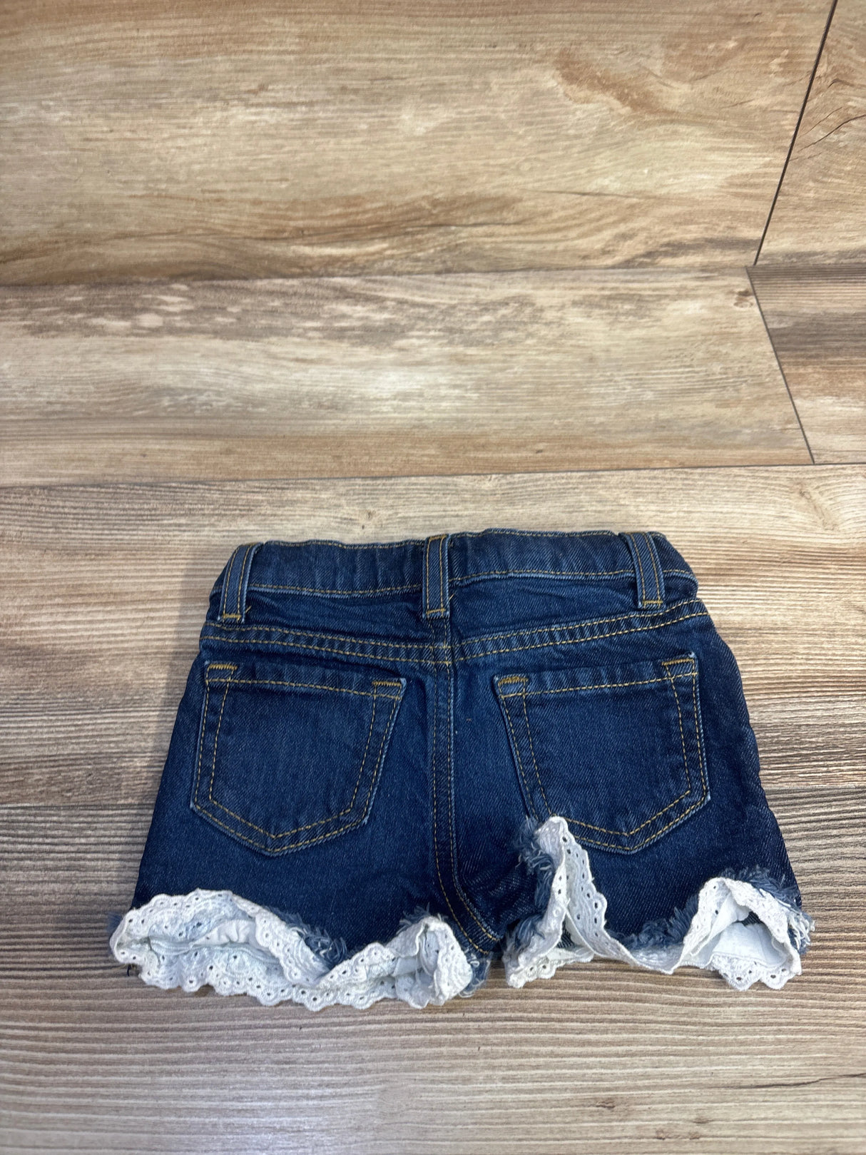 Back view of Cat & Jack denim toddler shorts showcasing eyelet lace trim and frayed hem on wood floor background