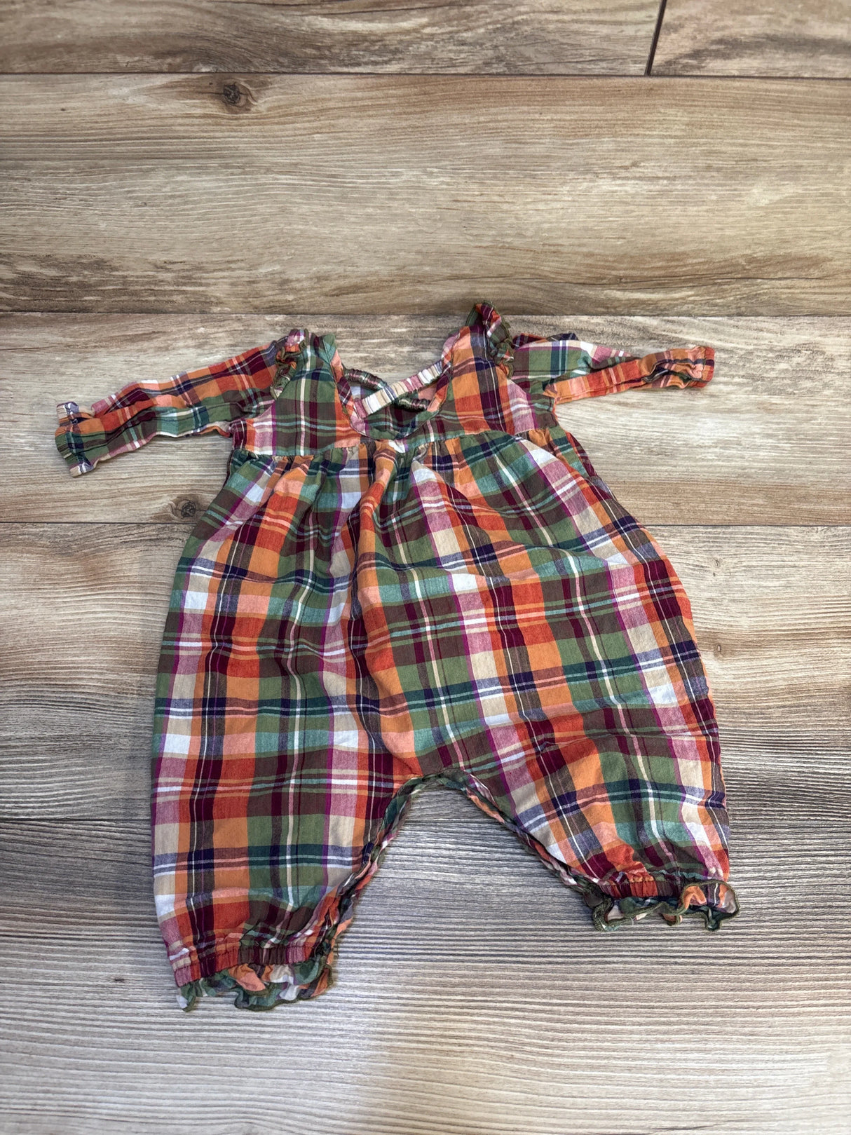 Plaid long sleeve baby romper in red, green, and orange on wood background