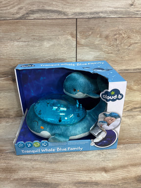 Front three-quarter view of Tranquil Whale blue plush projector nightlight showing blue projection dome in its Cloud b box on wood background
