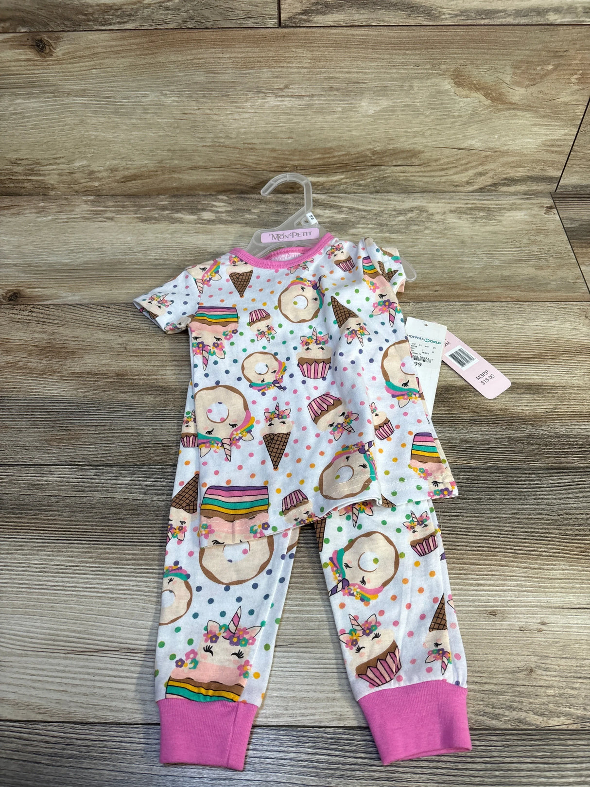 Kids' unicorn-themed pajama set with donuts and cupcakes, pink cuffs, on wooden floor