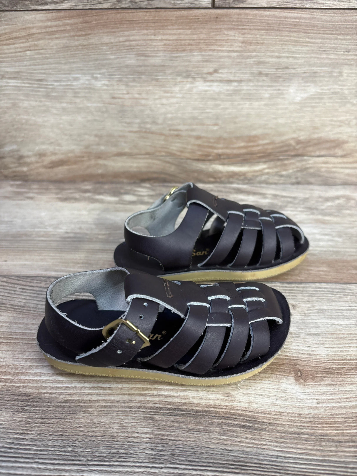 Side view of Salt Water Sun-San brown sandals size 7C showing woven straps, buckle and crepe sole on wood background