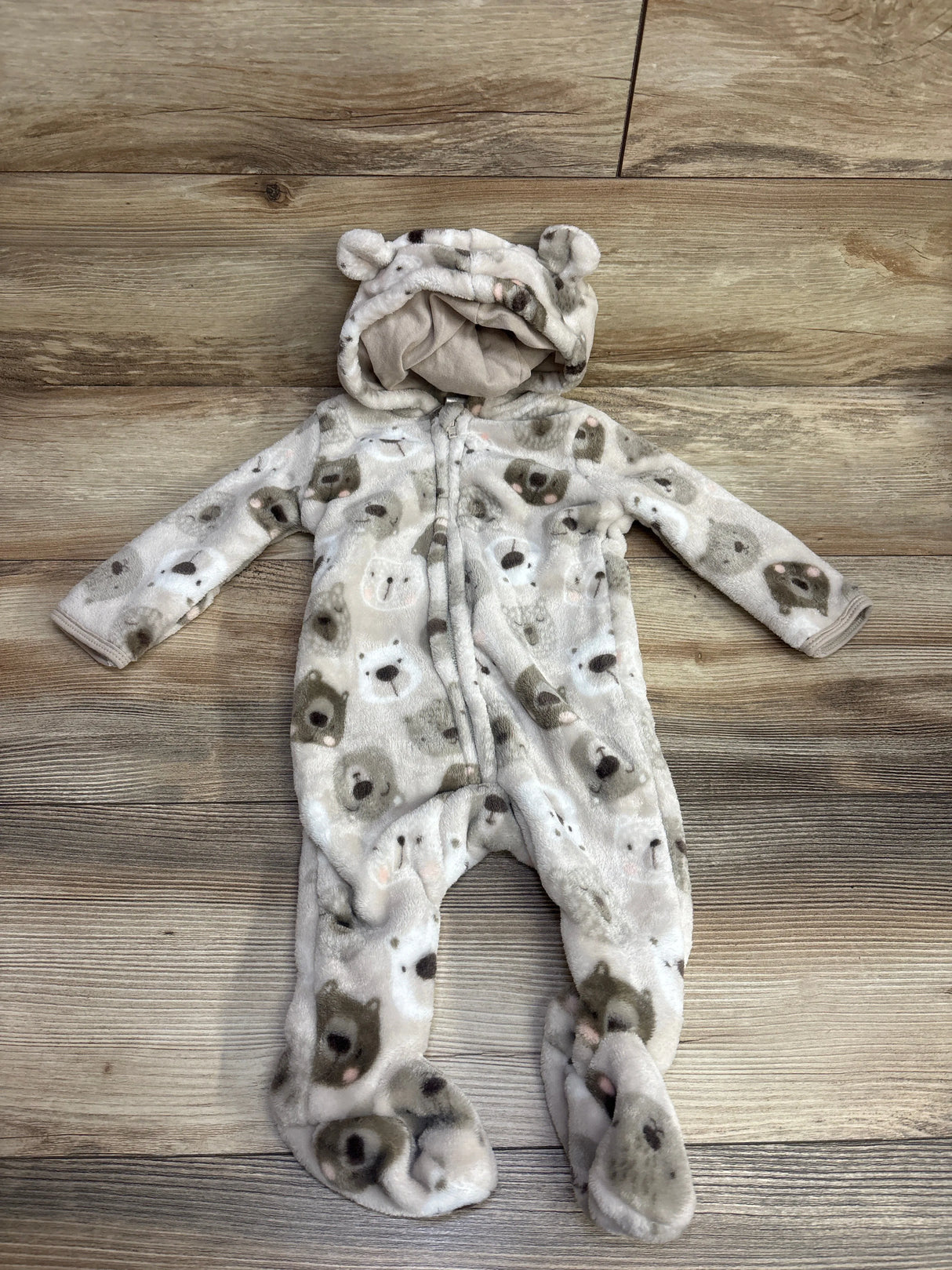 Soft baby fleece onesie with bear faces print and hood featuring bear ears, laid flat on wood floor