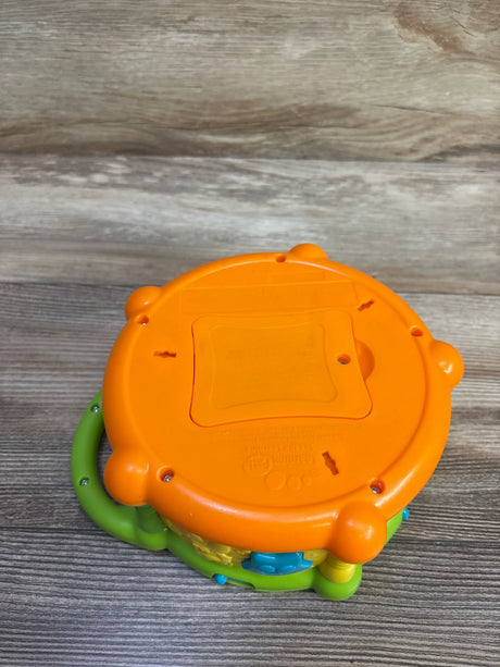 Underside view of LeapFrog Learn & Groove Color Play Drum showcasing orange battery cover and green handle on a wood surface