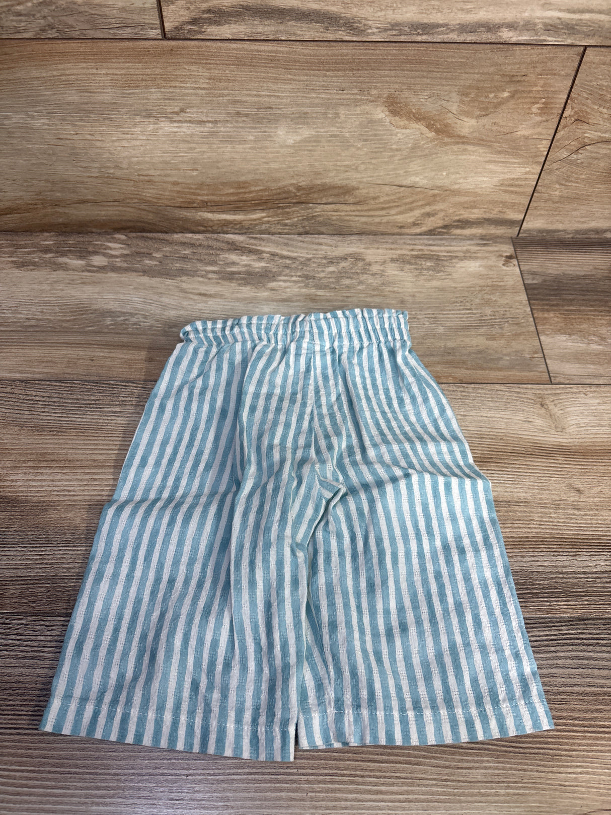 Front view of toddler blue-and-white striped Mayoral pants with elastic waistband on wood floor background