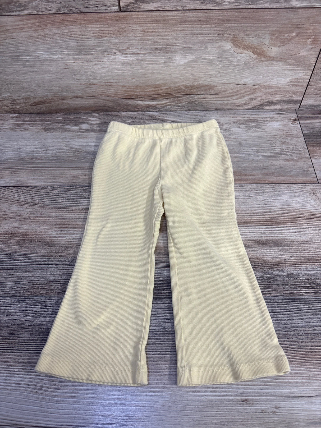 Flat lay of Baby Gap yellow ribbed flare leggings showing elastic waistband and flared legs on light wood background