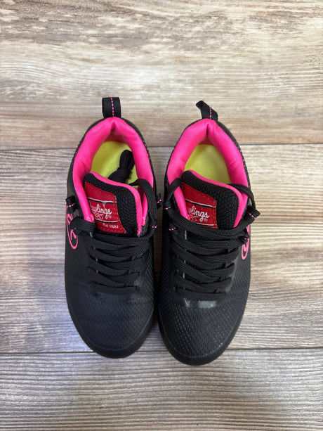 Top view of Rawlings girls softball cleats showcasing black uppers with pink lining and accents on a wood background