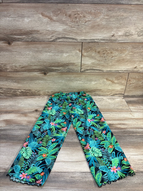Flat lay of teal tropical children's swim cover-up pants (size 4/5T) showing elastic waistband, wide legs, and lettuce-edge hem on wood plank background