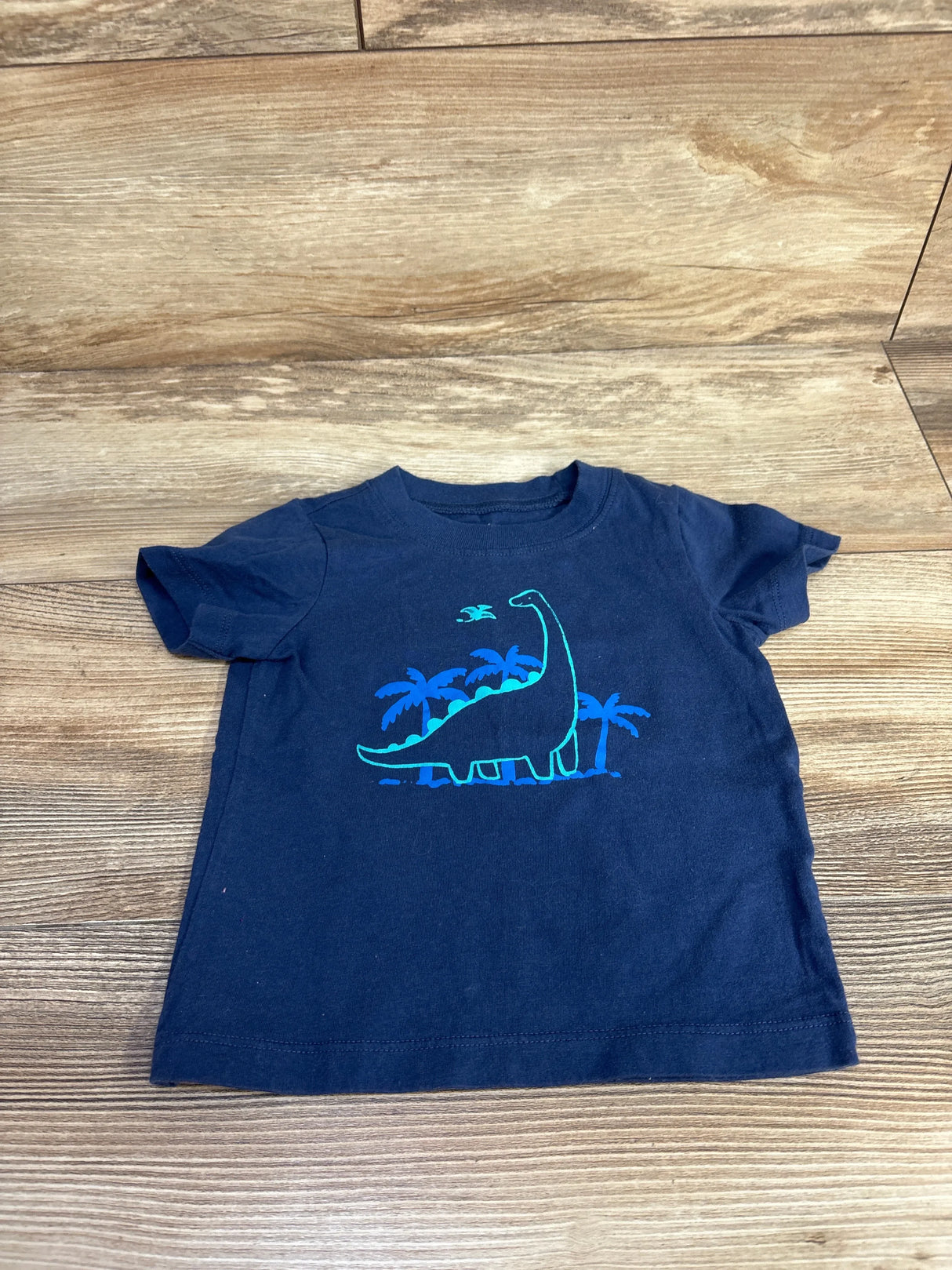 Front view of navy toddler t-shirt 18-month showing teal dinosaur and palm tree graphic on wood background