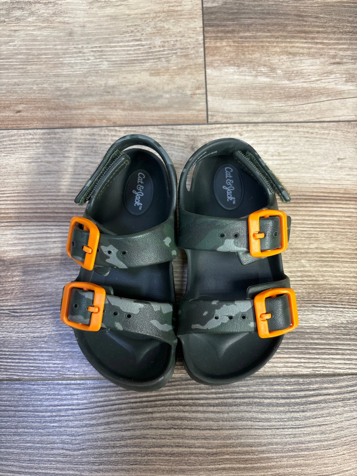 Top view of Cat & Jack kids camo footbed sandals showcasing two adjustable straps with bright orange buckles on wood floor