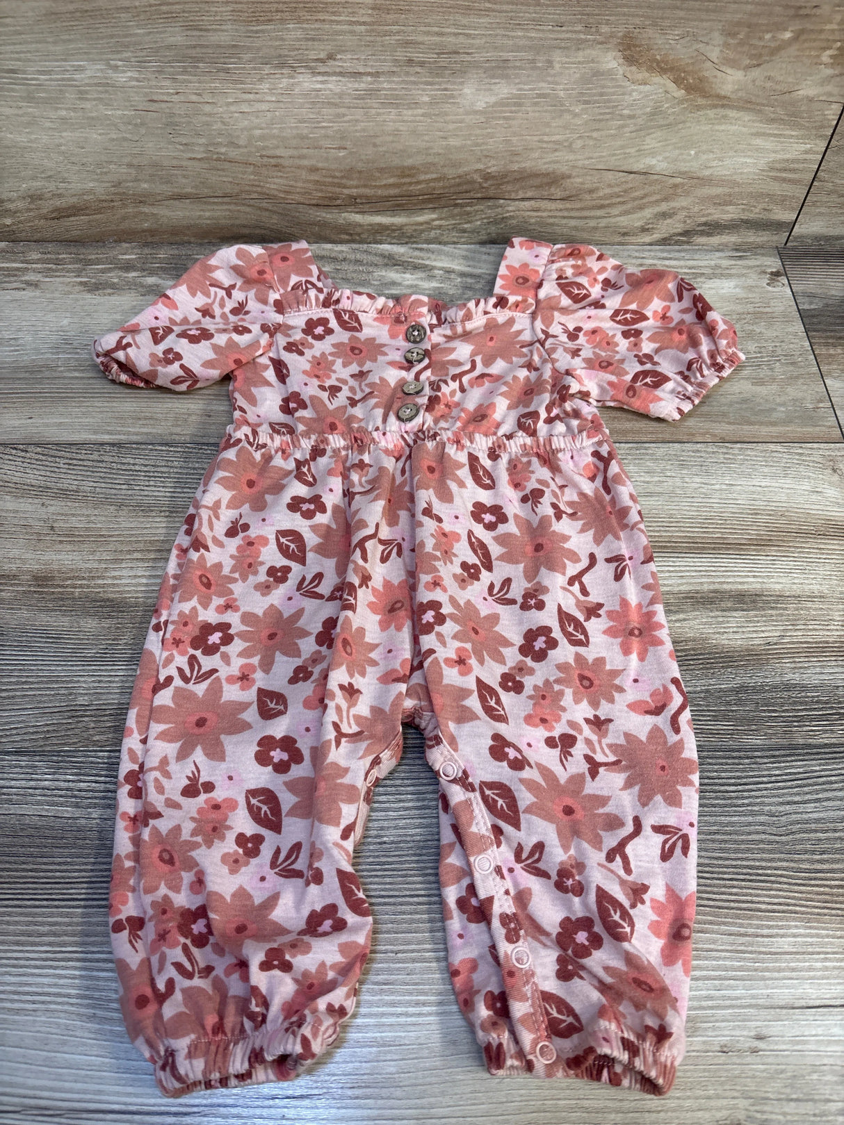 Pink floral long-sleeve baby romper with front buttons, displayed on wood floor