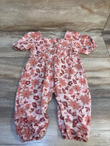 Pink floral long-sleeve baby romper with front buttons, displayed on wood floor