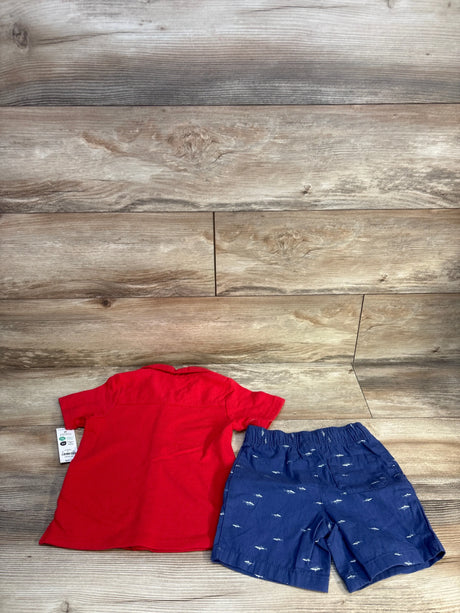 Red short sleeve toddler shirt and blue shorts with white shark print on wood background