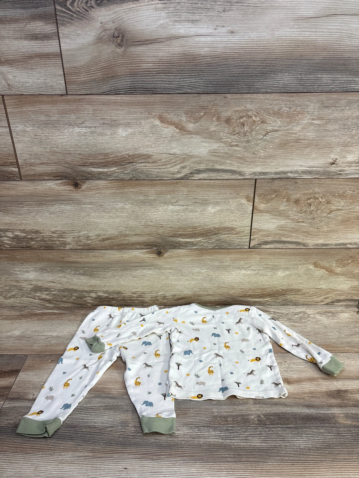 Top-down view of Mori Baby two-piece ivory safari pajama set (9–12 months) showing long-sleeve top and pants with green cuffs and animal print on wood background