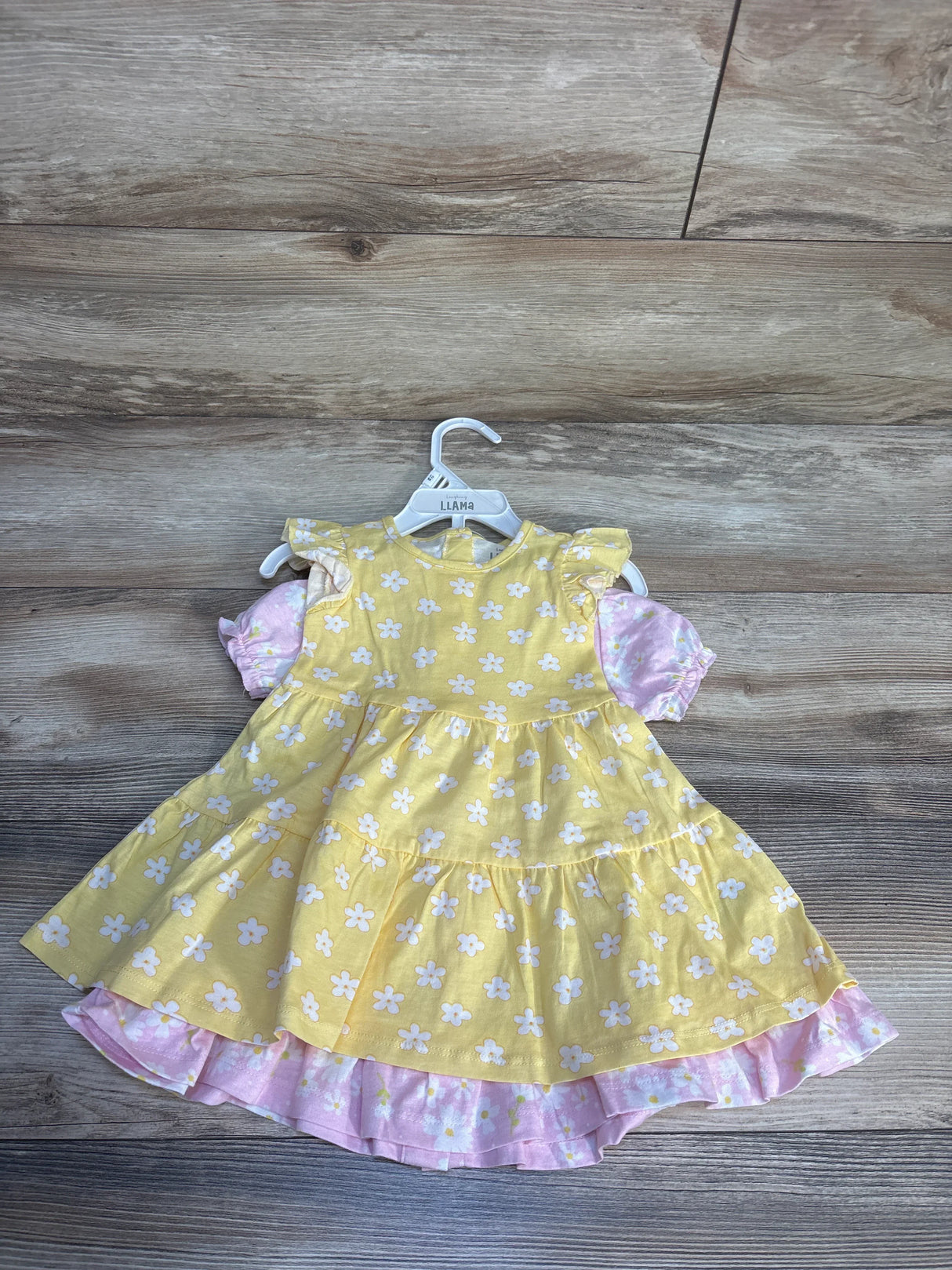 Yellow floral girls dress with pink ruffled hem and puff sleeves on wood background