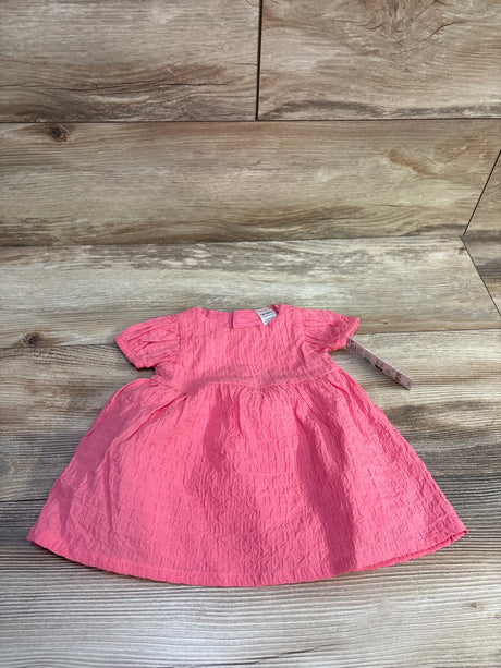 Flat lay of newborn pink crinkled cotton dress with matching bloomers, short puff sleeves and gathered skirt on wood background