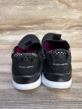 Black Skechers kids slip-on shoes with white soles, polka dot lining, on wood floor