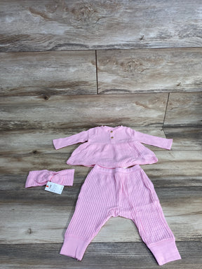 Top-down view of Cat & Jack 3-piece pink waffle-knit shirt and pants set (3-6M) showing long-sleeve peplum top with two buttons, elastic-waist cuffed pants, and matching headband on wood floor
