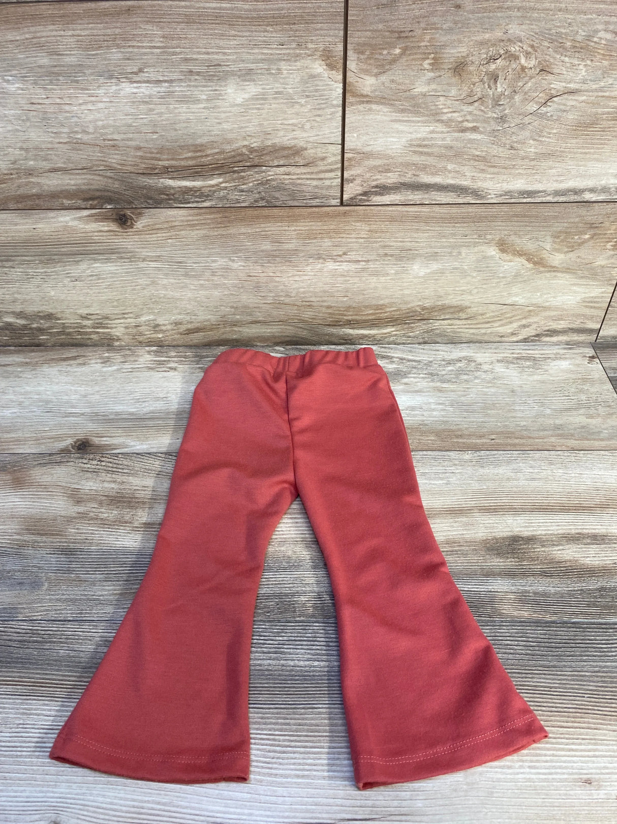 Flat lay of red toddler flared pants showing elastic waistband and wide flared legs on wood background