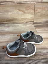 Three-quarter view of Munchkin by Stride Rite toddler gray sneakers with hook-and-loop strap and brown heel tab on wood floor