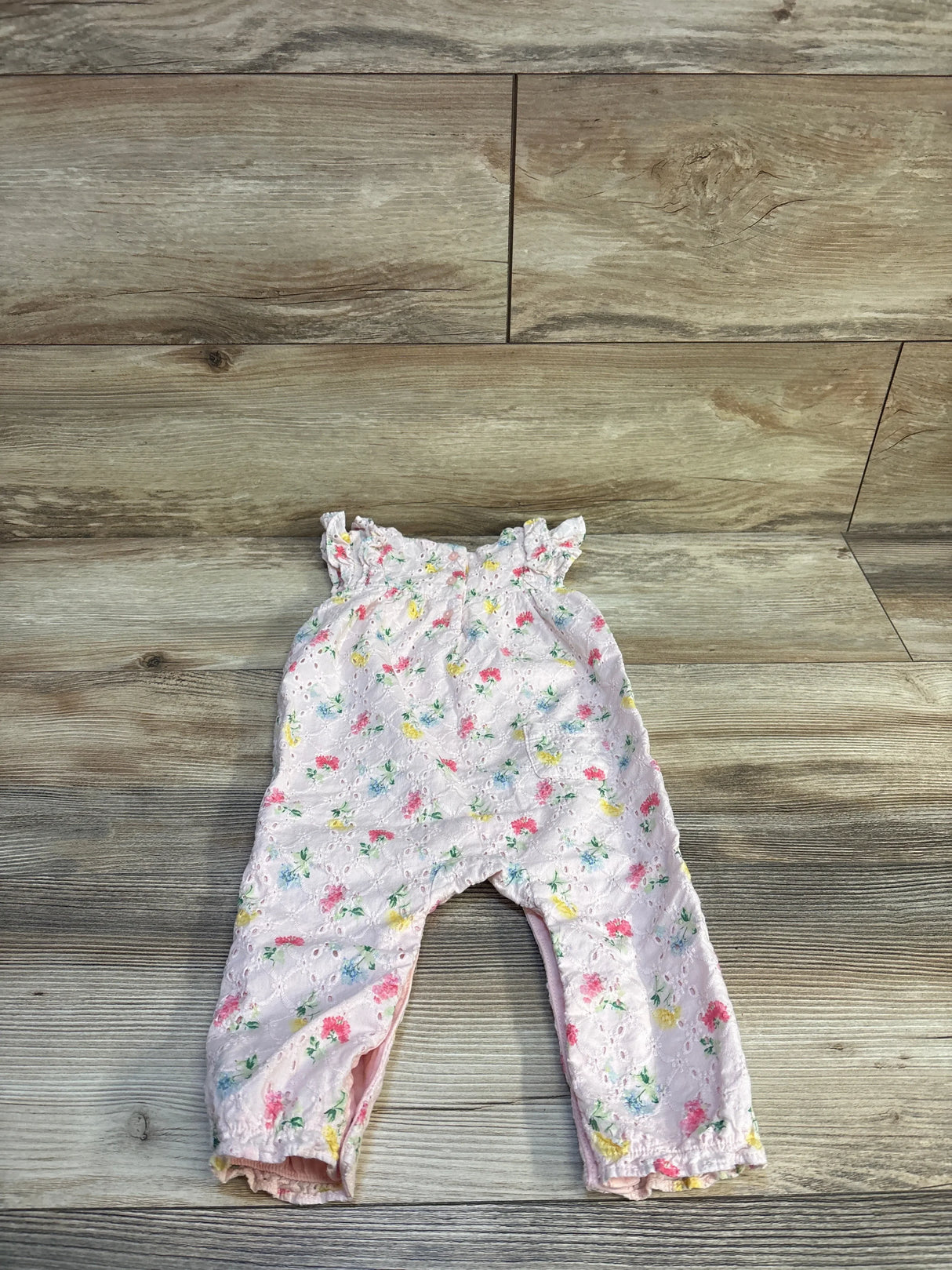 Flat lay of Janie and Jack floral eyelet ruffle jumpsuit in pink with multicolor flowers and ruffle straps on wood plank floor