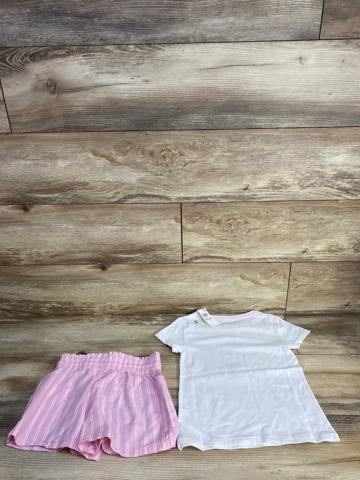 Flat lay of toddler set with white short-sleeve tee and pink striped elastic-waist shorts on wood background