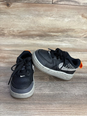 Pair of black and gray toddler Nike sneakers with orange heel tabs on wood background