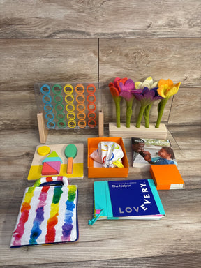 Front view of Lovevery The Helper play kit with activity board, wooden puzzle pieces, felt flowers and cloth book