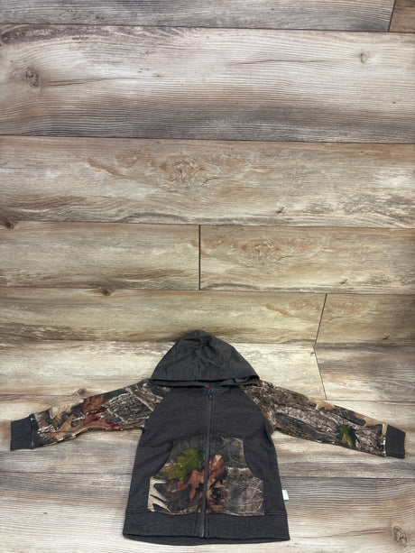 Front view of Outdoor Kids camo zip-up jacket showcasing a hood, camouflage sleeves and front panels on a wood background