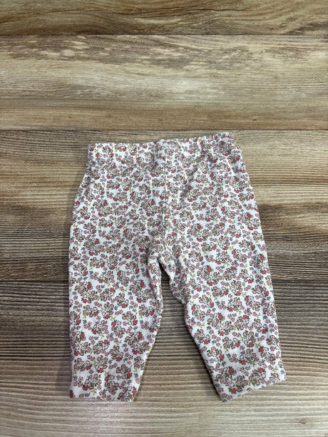 Front view of Child Of Mine floral pants in white, size 0 to 3 months, with an allover floral print on a wood background