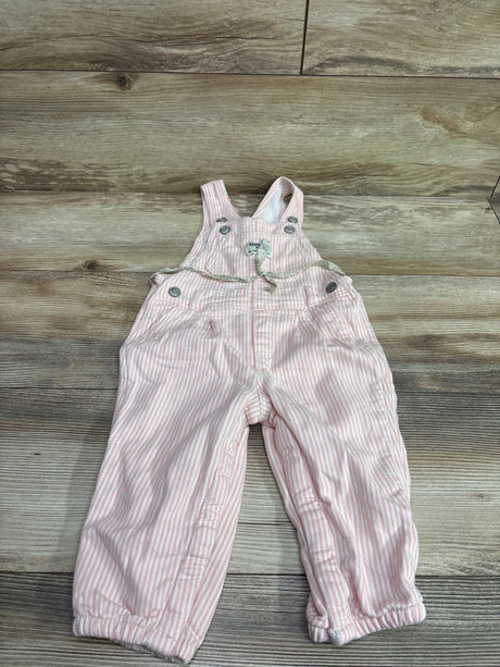 Front view of Oshkosh pink and white striped overalls in size 18 months with bib straps, buttons, pockets, and elastic cuffs on a wood floor