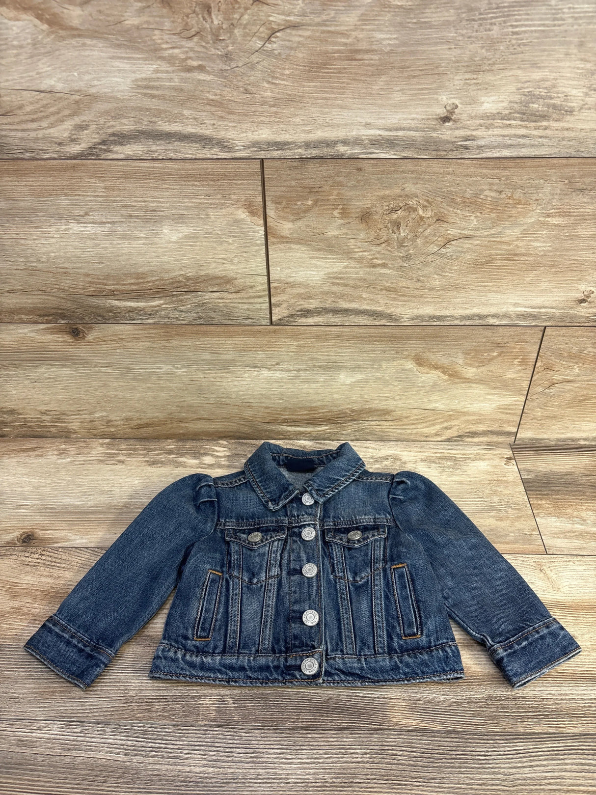 Front view of Baby Gap Minnie toddler denim jacket 12-18m with button-front, puff shoulders on wood background