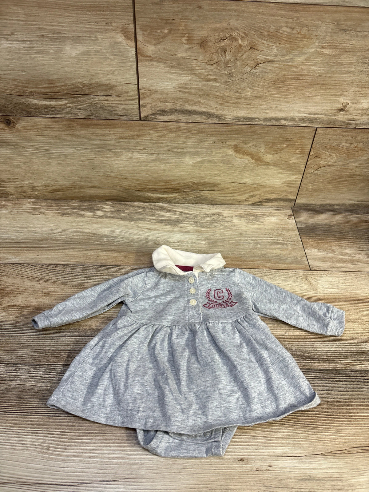Front view of Carter’s grey polo bodysuit dress, size 3m, with long sleeves, collar, and attached bottom on wood floor