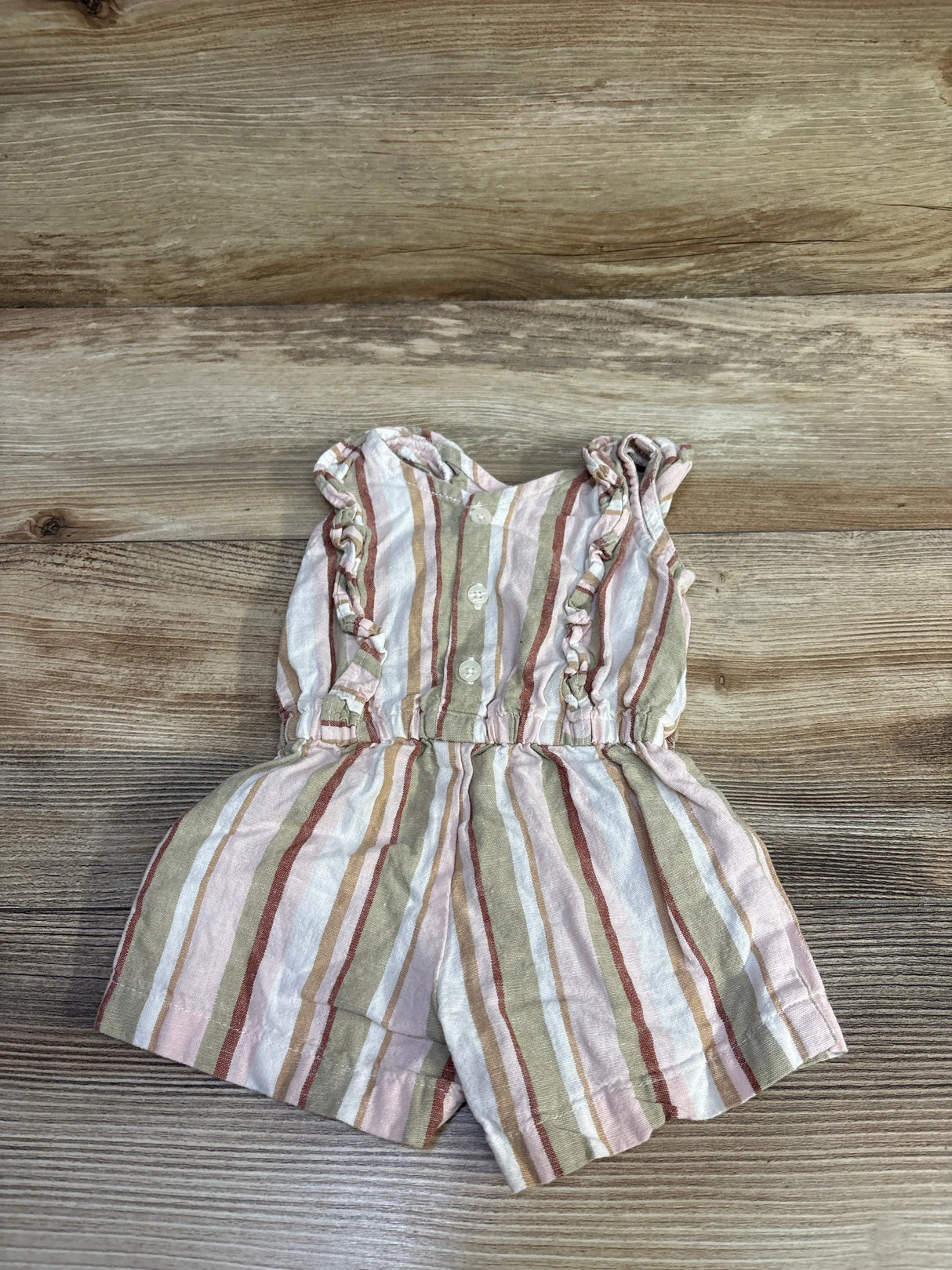 Flat lay of striped shortie romper in white and pink with ruffle shoulders, buttons and elastic waist on wood background